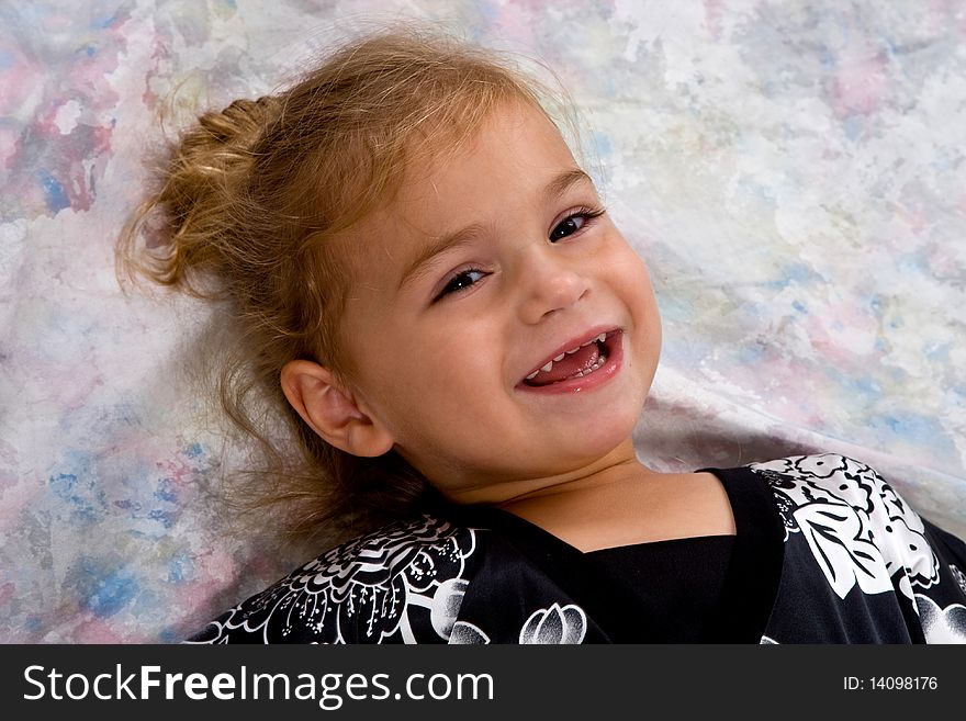 Portrait of a pretty little blond headed girl smiling.  She is lying on a painted background. Portrait of a pretty little blond headed girl smiling.  She is lying on a painted background.