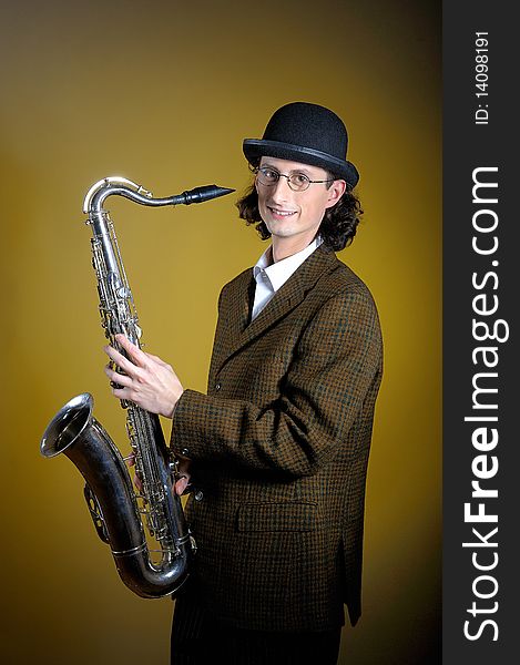 Portrait of young english gentleman in bowler hat holding saxophone. yellow background. Portrait of young english gentleman in bowler hat holding saxophone. yellow background