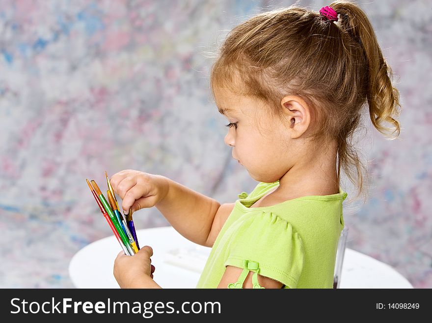 Cute little girl in green blouse picking out the right water color brush for her painting. Cute little girl in green blouse picking out the right water color brush for her painting.