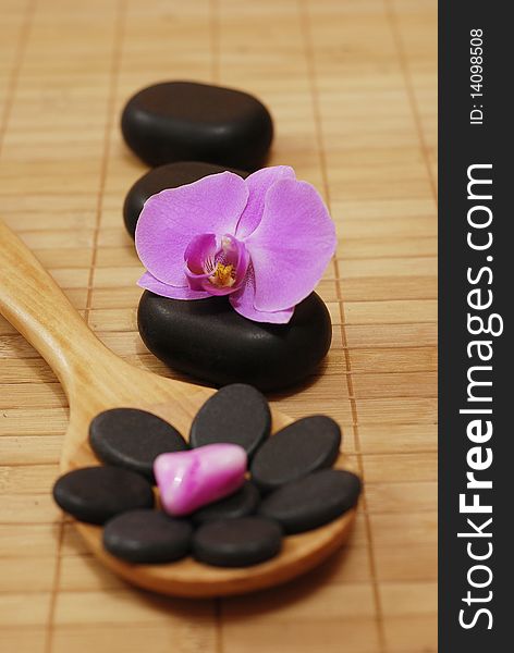 Wooden spoon with stones and the flower of the orchid on the bamboo mat. Wooden spoon with stones and the flower of the orchid on the bamboo mat