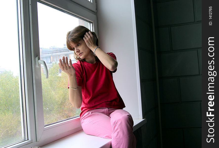 The woman sits on a window sill, smokes and talks. The woman sits on a window sill, smokes and talks