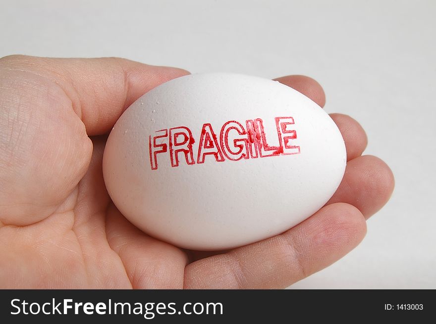 Hand holding a white egg that is stamped fragile. Hand holding a white egg that is stamped fragile.