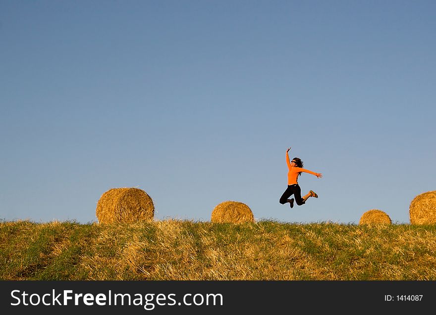 Woman jumping in a hay bales field