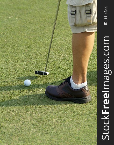 Foot and putter of a man putting on a golf green. The ball has motion blur. Focus on the club-head. Foot and putter of a man putting on a golf green. The ball has motion blur. Focus on the club-head.