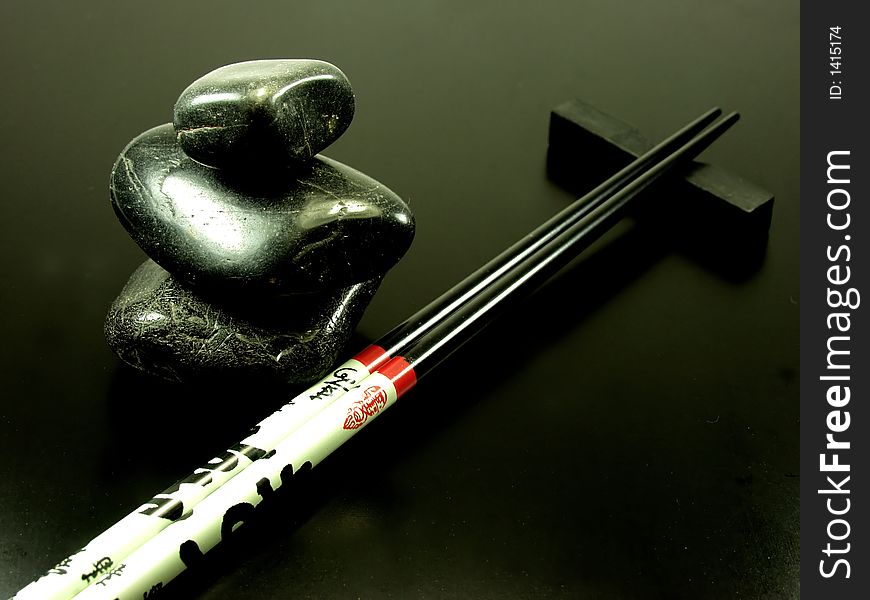 Black hot stones whit decorated chopsticks on black background. Black hot stones whit decorated chopsticks on black background