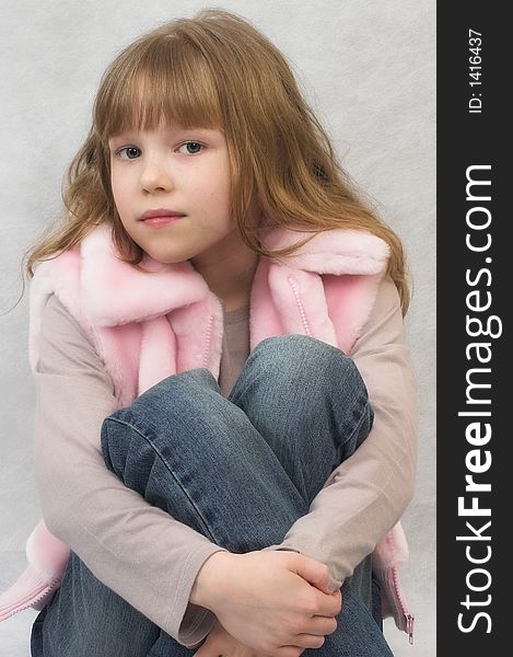 Young girl sits. She wears T-shirt, pink vest and jeans. Young girl sits. She wears T-shirt, pink vest and jeans.