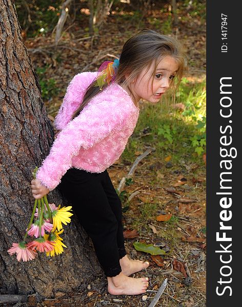 A little girl standing by a tree barefoot holding a bouquet of daisies she just picked from the garden. A little girl standing by a tree barefoot holding a bouquet of daisies she just picked from the garden.
