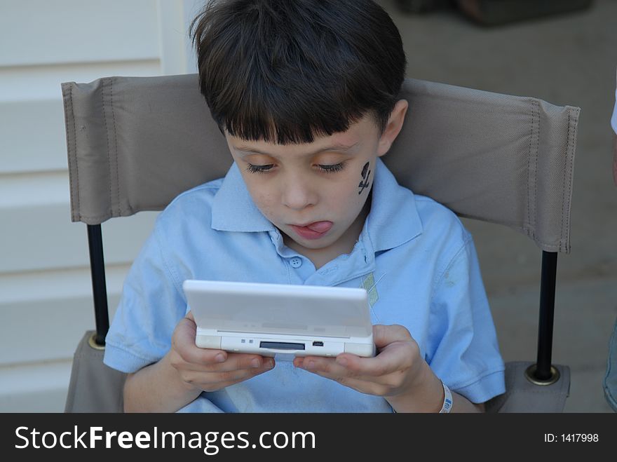 A young boy playing his electronic game with much intensity with a funny expression on his face. A young boy playing his electronic game with much intensity with a funny expression on his face