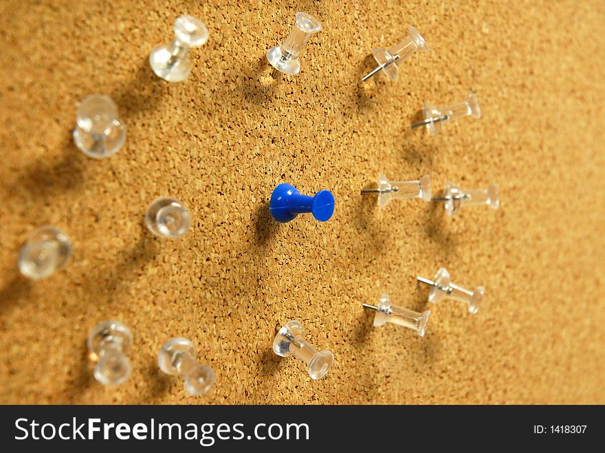 A blue push-pin in the center of many clear ones on a bulletin board. A blue push-pin in the center of many clear ones on a bulletin board.