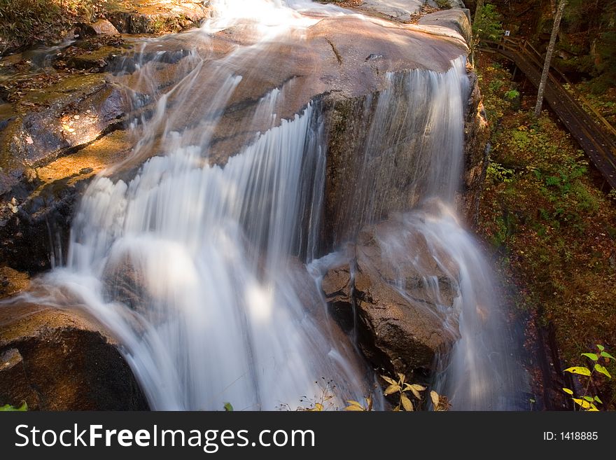 The river flows over a large boulder creating a waterfall around the entire rock. The river flows over a large boulder creating a waterfall around the entire rock.