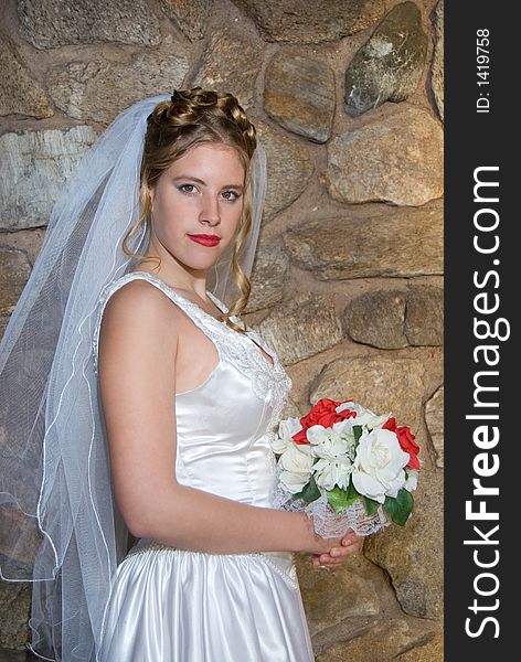 Autumn Bride with bouquet in front of stone wall.