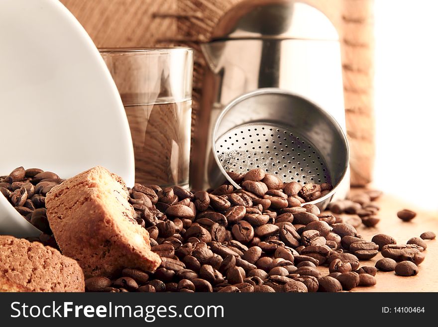 A white cup, cookies, a glass of water and a pot encircled by coffee beans. A white cup, cookies, a glass of water and a pot encircled by coffee beans.