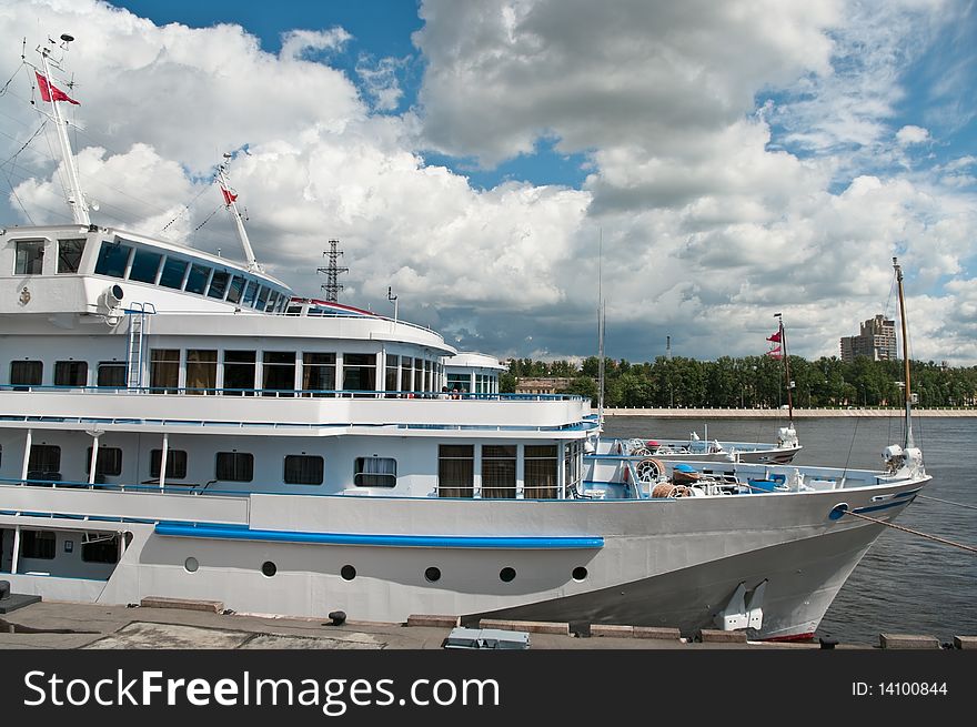 White cruise liner is moored in river port. Saint-Petersburg, Neva river. Blue sky with clouds.