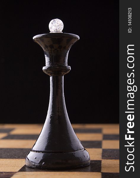 Black chess queen stands on a chessboard, black background