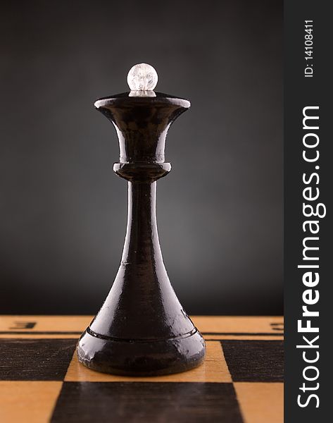 Black chess queen stands on a chessboard, black background