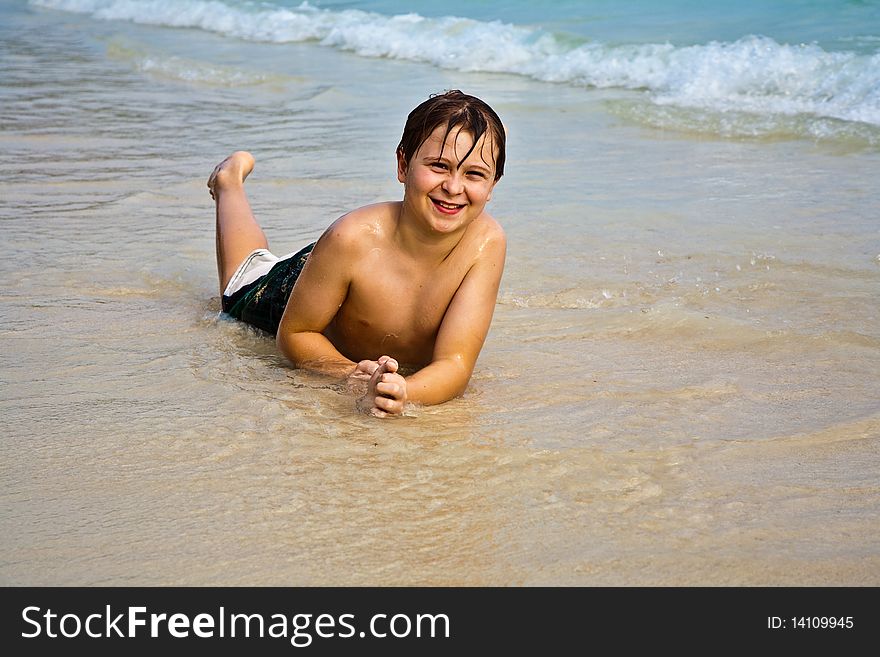 Young boy is lying at the beach and enjoying the warmness of the water and looking self confident and happy. Young boy is lying at the beach and enjoying the warmness of the water and looking self confident and happy