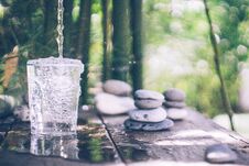 Clean Water Pouring Into The Glass Next To The Stones On The Old Table. Japanese Style Stock Photo