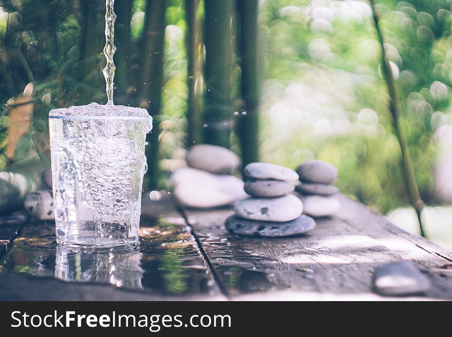 Clean Water Pouring Into The Glass Next To The Stones On The Old Table. Japanese Style