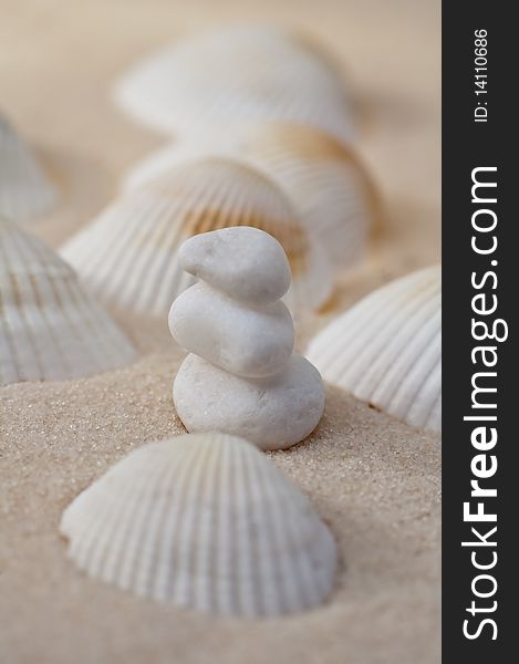 Three stacked white stones on a sand between several white sea-shells. Three stacked white stones on a sand between several white sea-shells