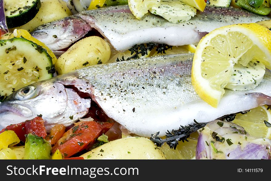 Fresh whole rainbow trouts on a bed of vegetables, ready to be cooked