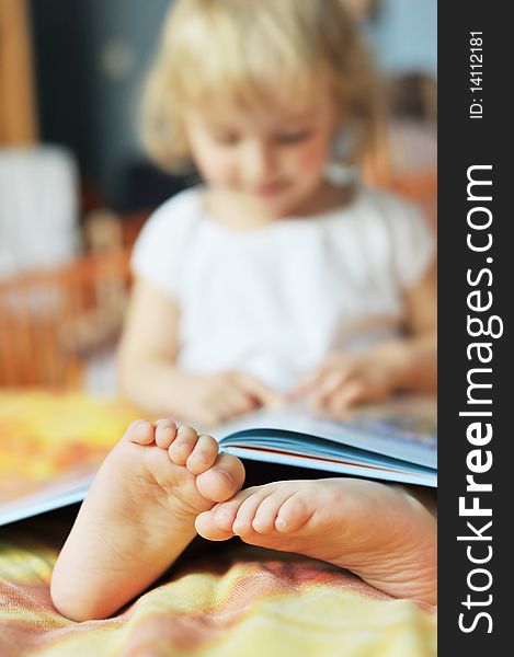 Cheerful little girl with book sits on bed of parents