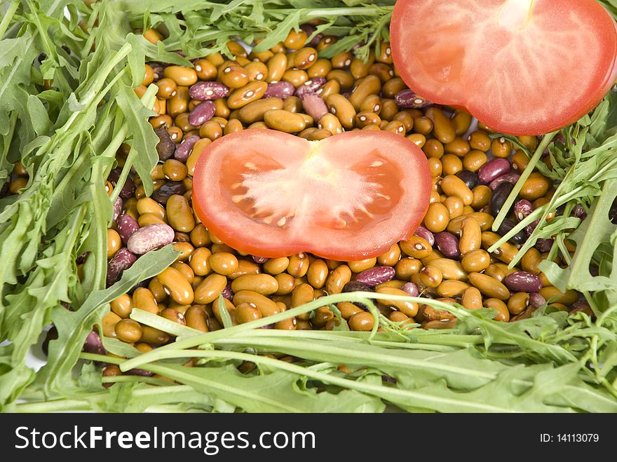 Sliced tomatoes on beans, surrounded arugula close-up. Sliced tomatoes on beans, surrounded arugula close-up