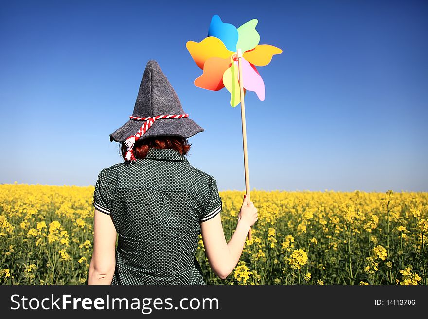 Girl in cap with wind turbine at rape field.