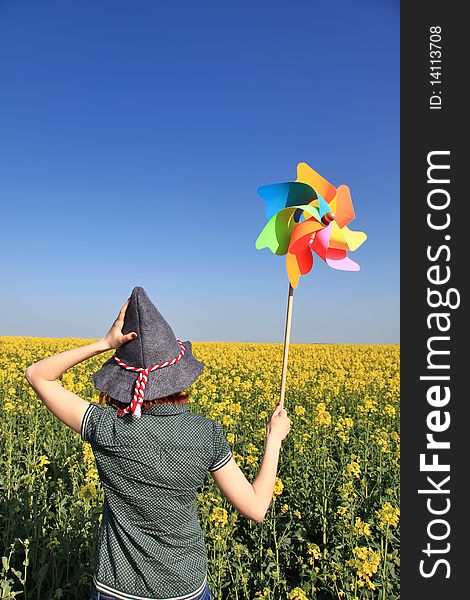 Girl in cap with wind turbine at rape field.