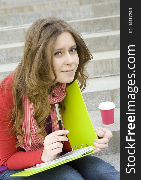 Beautiful student sitting on the concrete stairs of the University. On his knees lay a folder with synopses next cup of coffee. Lunch. Beautiful student sitting on the concrete stairs of the University. On his knees lay a folder with synopses next cup of coffee. Lunch