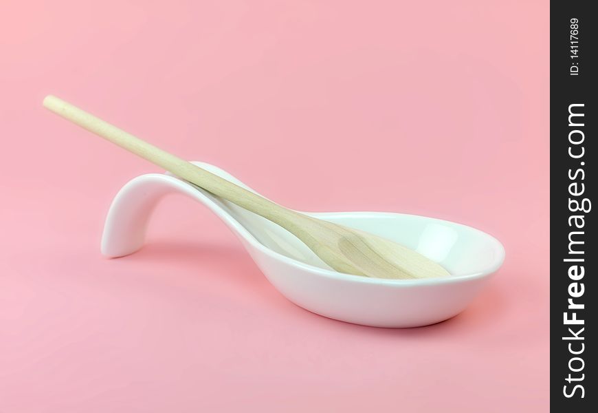 A wooden spoon in a resting laddle isolated against a pink background. A wooden spoon in a resting laddle isolated against a pink background