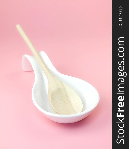 A wooden spoon in a resting laddle isolated against a pink background. A wooden spoon in a resting laddle isolated against a pink background