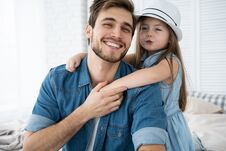 Portrait Of Handsome Father And His Cute Daughter Hugging, Looking At Camera And Smiling While Sitting On Sofa At Home. Royalty Free Stock Photo Portrait Of Handsome Father And His Cute Daughter Hugging, Looking At Camera And Smiling While Sitting On Sofa At Home. Royalty Free Stock Photo
