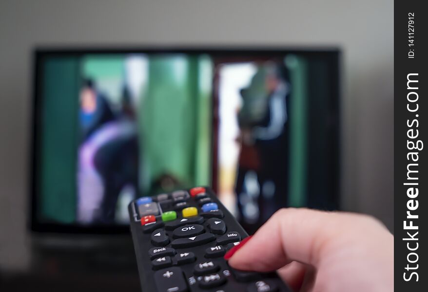 Female Hand With Remote Control On The Background Of The TV