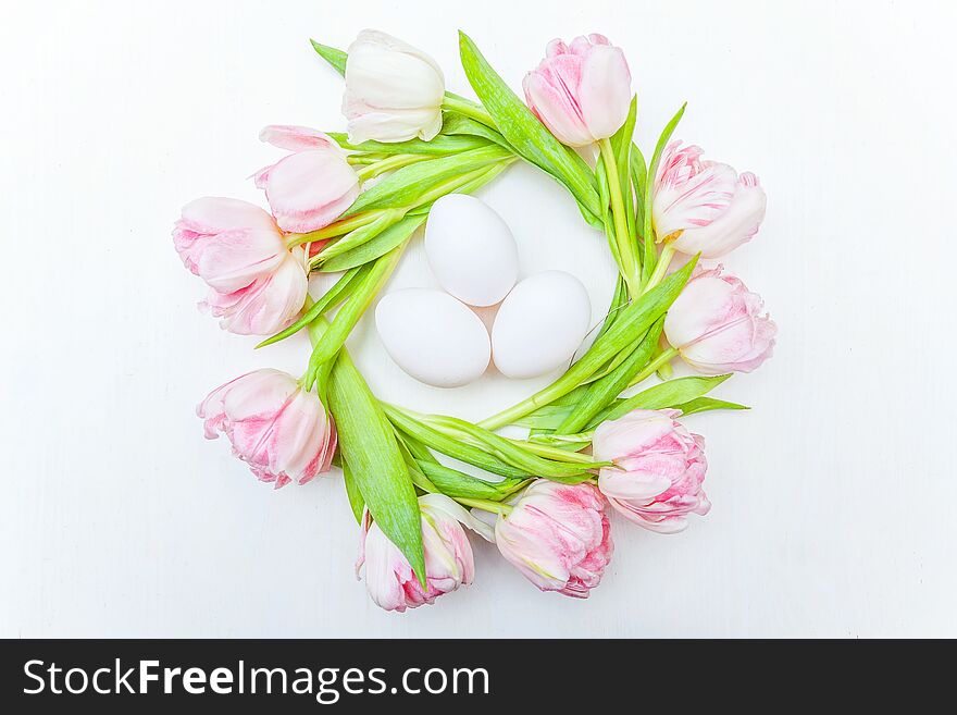 Easter eggs in nest and pink fresh tulip bouquet on rustic white wooden background