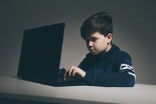 Photo Of Nice Boy In Sweater Sitting Infront Of The Computer Doing Homework. Royalty Free Stock Image