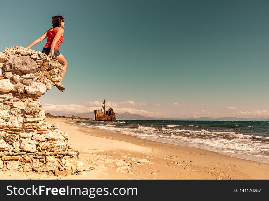 Travel freedom. Mature tourist woman on beach enjoying summer vacation. An old abandoned shipwreck, wrecked boat in the background. Travel freedom. Mature tourist woman on beach enjoying summer vacation. An old abandoned shipwreck, wrecked boat in the background