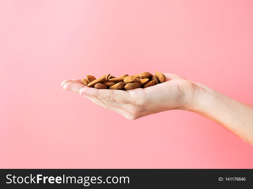 Young woman hand holding almonds on pink background