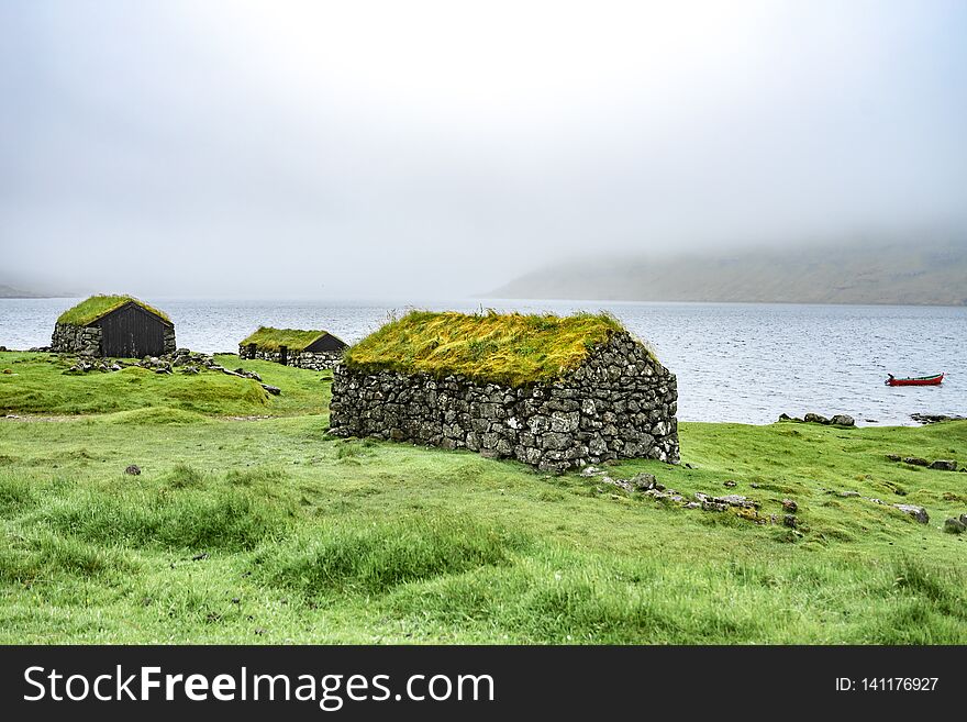 Beautiful fisherman rock house with green grass on the roof, sea side next to blue ocean with boat in the background foggy weather