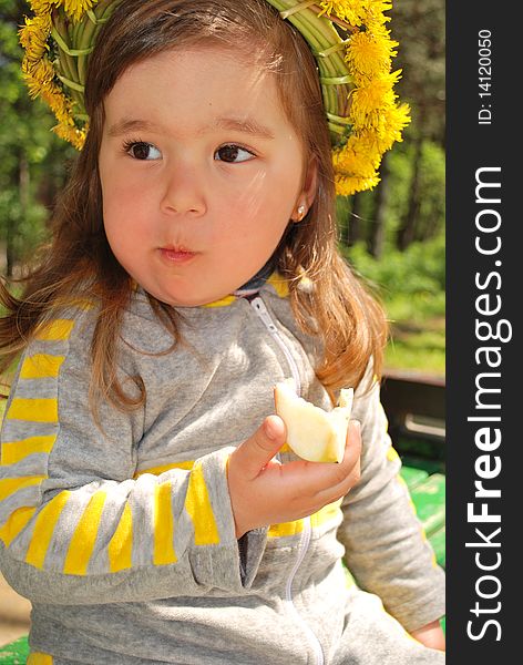 Little girl wearing dandelion diadem eating a slice of apple. Little girl wearing dandelion diadem eating a slice of apple