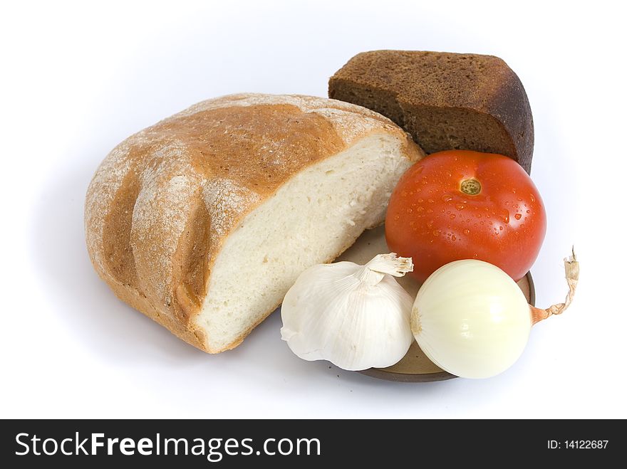 White and brown bread, and red ripe tomato, onion, garlic on a plate, isolated on the white background. White and brown bread, and red ripe tomato, onion, garlic on a plate, isolated on the white background