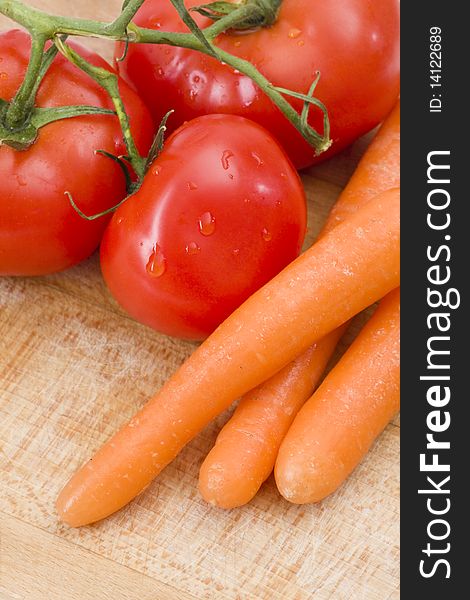 Fresh tomatoes and carrot on wooden cutting board