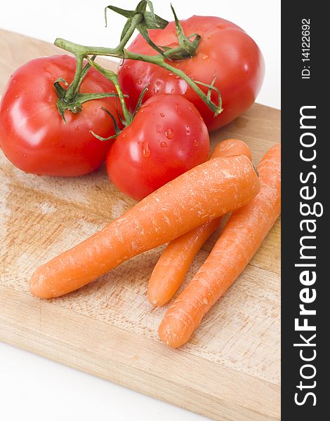 Fresh tomatoes and carrot on wooden cutting board