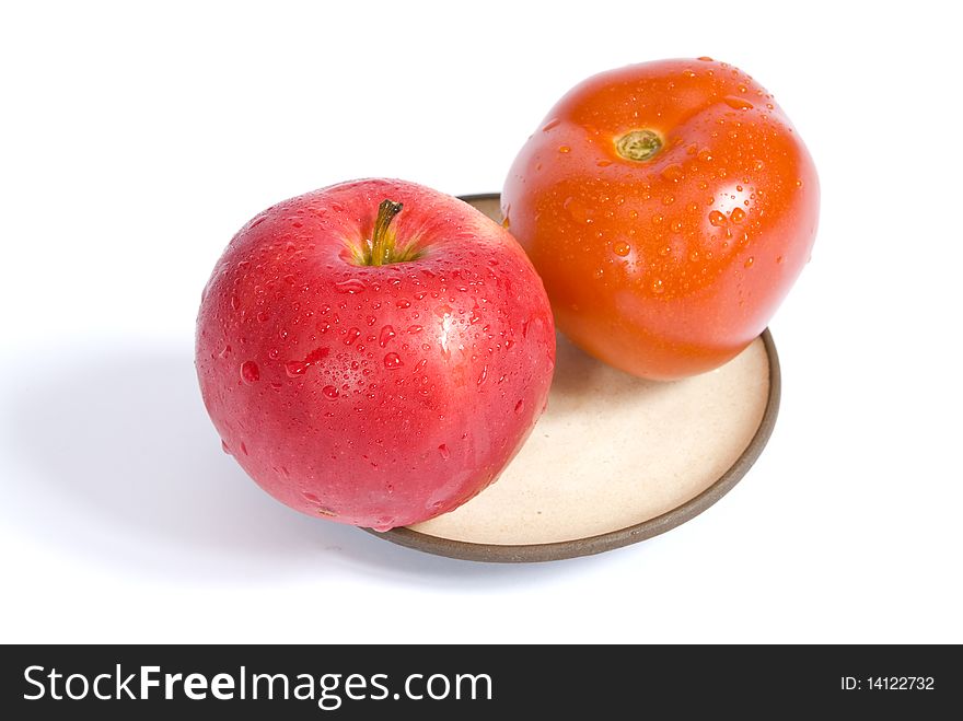 Red ripe tomato and apple, covered with water droplets, on a plate, isolated on white background