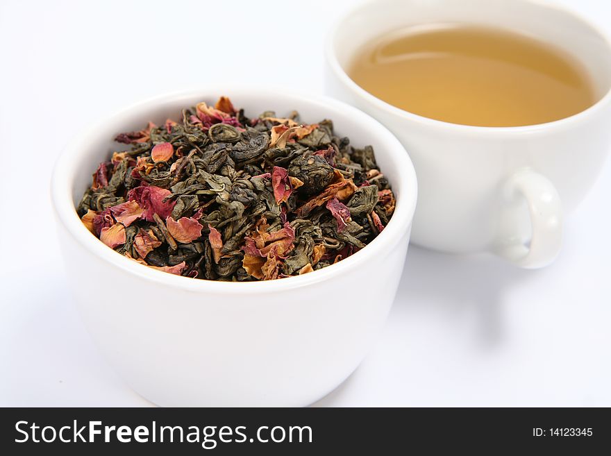 Bowl filled with dried green tea leaves and rose petals and a cup of green tea