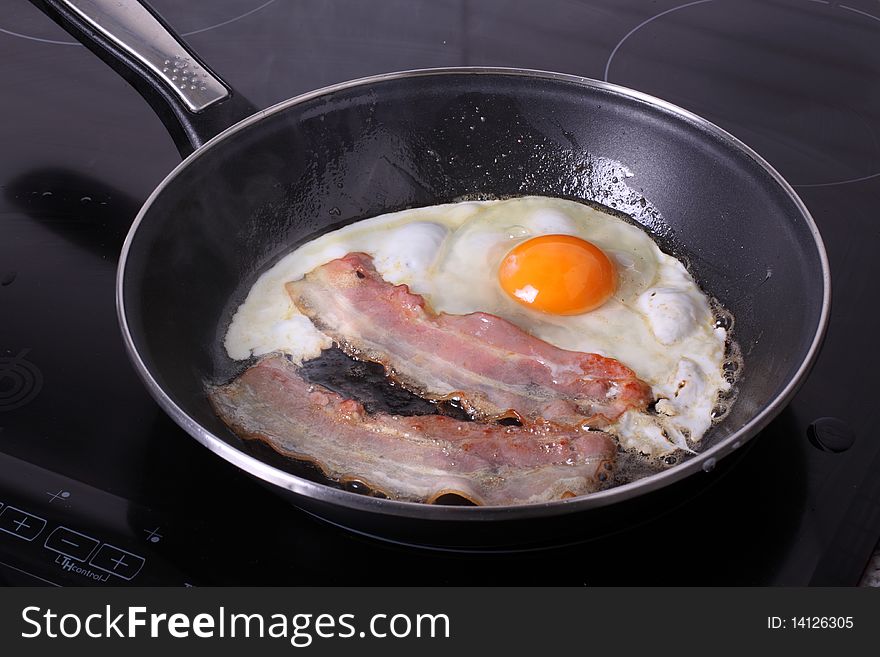 Bacon and eggs being cooked in a fryer