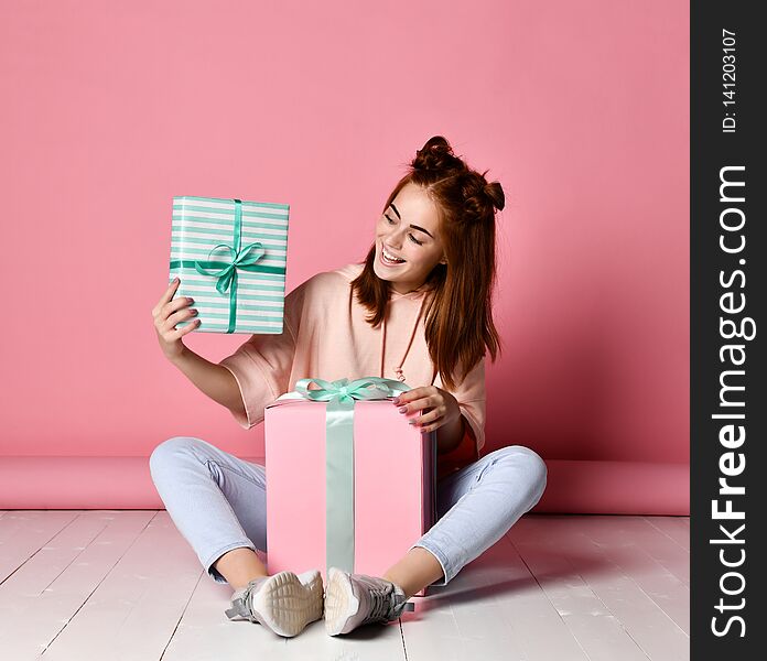 Portrait of a smiling red head woman sitting on a floor with lots of gift boxes and having fun over pink background. Portrait of a smiling red head woman sitting on a floor with lots of gift boxes and having fun over pink background