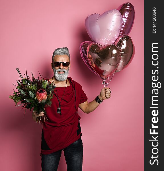 Stylish bearded middle-aged man with a modern hairstyle and fashionably dressed holding bunch of heart shaped balloons and a bouquet of flowers. Concept Valentine`s Day, Date. Stylish bearded middle-aged man with a modern hairstyle and fashionably dressed holding bunch of heart shaped balloons and a bouquet of flowers. Concept Valentine`s Day, Date