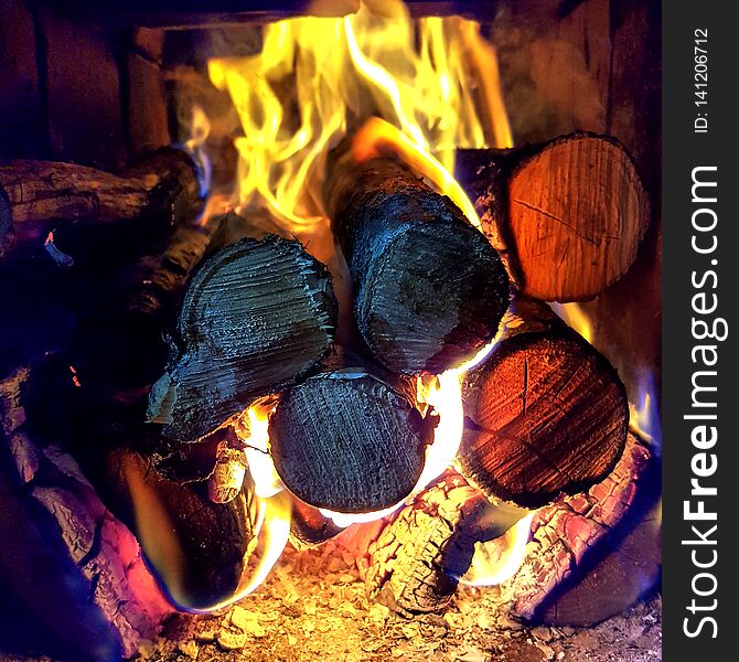 Fire flame burning coal and wood in open fireplace: charred timber and bright flames blaze on dark background. Fire flame burning coal and wood in open fireplace: charred timber and bright flames blaze on dark background