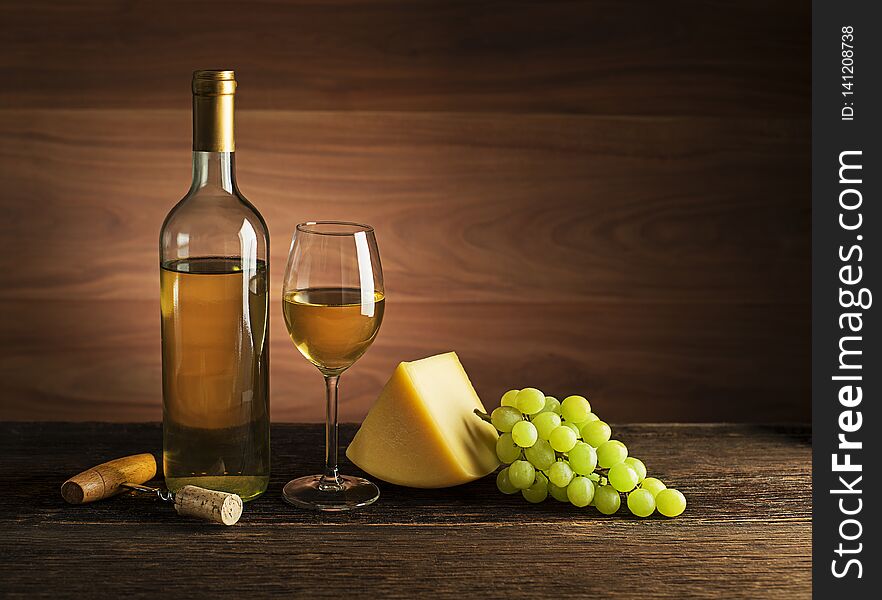 Bottle of white wine with snack food on old board. Glass of wine and cork with wooden background. Bottle of white wine with snack food on old board. Glass of wine and cork with wooden background