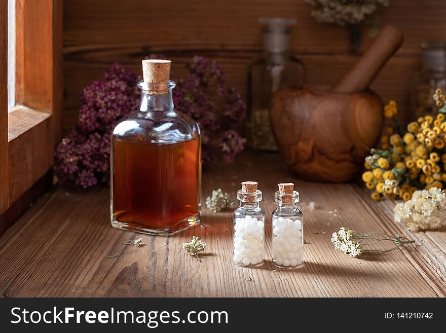 Two bottles of homeopathic globules with dried herbs and a tincture in the background. Two bottles of homeopathic globules with dried herbs and a tincture in the background